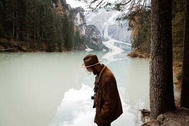 Seitenansicht eines Mannes in Freizeitkleidung, der stehend den Blick auf einen türkisfarbenen See mit nebligen Dolomitenbergen im Hintergrund in Italien genießt - ADSF10430