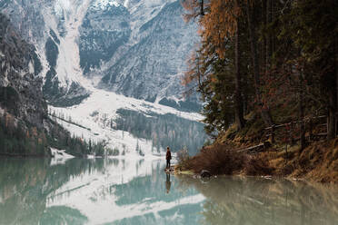 Side view of man traveler in casual wear standing and delighting in view of turquoise lake with foggy Dolomites mountains on background at Italy - ADSF10431