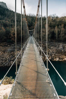 Leere schmale Fußgängerbrücke, die über einen Fluss führt und die rauen Felsen des Montsec-Gebirges in Spanien verbindet - ADSF10446