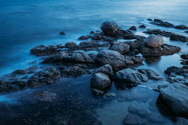 Dark island surrounded foamy waves under cloudy sky - ADSF10449