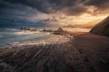 Scenic Blick auf leeren Strand mit Steinen und Wellen auf Sonnenuntergang Hintergrund mit regen Wolken - ADSF10475