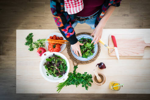 Anonyme Dame in bunter Jacke bereitet Gemüse zu, während sie in der Küche einen gesunden Salat zubereitet - ADSF10499