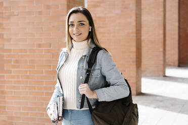 Lächelnder Universitätsstudent mit Tasche und Buch auf dem Campus - RDGF00048