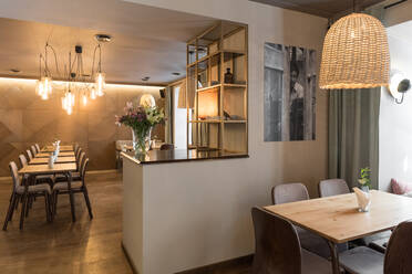 Stilvolle Lampe leuchtet über kleinen Tischen und bequemen Stühlen in einem gemütlichen Restaurant - ADSF10505