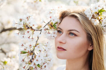 Attractive lady smiling and looking at camera while standing near tree branches blooming with white flowers - ADSF10517