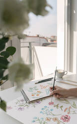 Crop Person Hand mit Pinsel malen Aquarell Blumen auf großen Blatt am Schreibtisch - ADSF10533