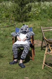 Junge im Zebrakostüm auf einem Stuhl sitzend auf einem Feld an einem sonnigen Tag - VPIF02632