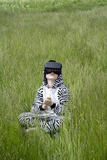 Junge im Zebrakostüm benutzt VR-Simulator, während er im Gras sitzt - VPIF02652