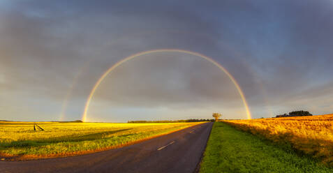 Doppelter Regenbogen, der sich über eine leere Landstraße wölbt - SMAF01965