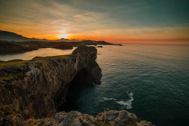 Panoramablick auf riesige Felsenklippen über dem gekräuselten Wasser vor dem Himmel bei Sonnenuntergang, Asturien, Spanien - ADSF10568