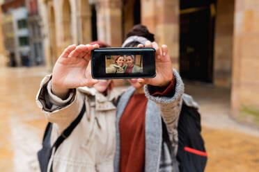 Ausgeglichene fröhliche multiethnische Frauen, die ein Selfie mit dem Handy machen und das Foto in die Kamera auf der Straße halten - ADSF10654