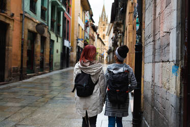 Rückenansicht von aktiven touristischen Frauen mit Rucksack zu Fuß entlang leeren Straßen in der Stadt - ADSF10658