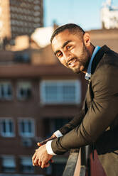 Young male professional leaning on railing at rooftop in city - EHF00775