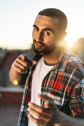 Handsome young man pointing while standing on rooftop in city - EHF00785