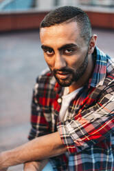 Confident young man wearing plaid shirt at rooftop in city - EHF00787