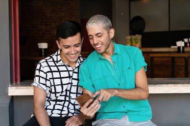 Schwuler Mann zeigt auf sein Handy, während er es mit einem Freund teilt, während er am Tresen eines Restaurants sitzt - SPCF00830
