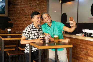 Young gay couple taking selfie while drinking beer at bar - SPCF00831