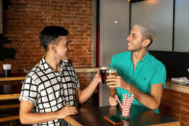Gay couple toasting beer while standing at table in bar - SPCF00833