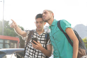 Junger Mann, der auf einen Freund zeigt, während er sein Smartphone zur Orientierung in der Stadt benutzt - SPCF00849