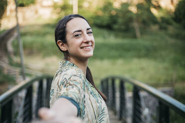 Happy woman standing over footbridge in public park - XLGF00449