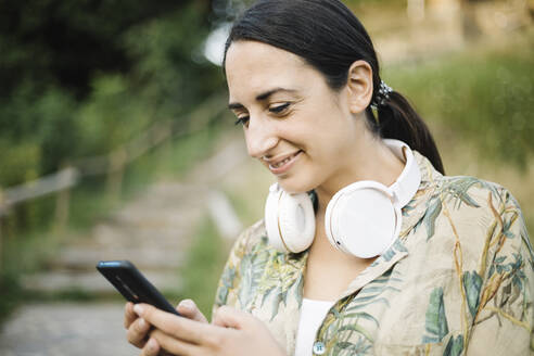 Frau lächelt, während sie eine Textnachricht auf ihrem Smartphone schreibt - XLGF00452