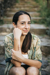 Smiling woman sitting on steps at park - XLGF00455