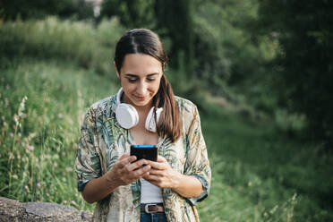 Lächelnde Frau, die mit ihrem Smartphone im Park Nachrichten schreibt - XLGF00459