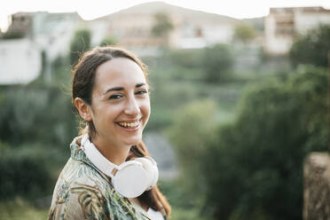 Smiling woman with headphones standing in public park - XLGF00462