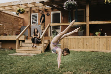 Mädchen macht Akrobatik im Garten, Eltern auf der Terrasse - SMSF00161