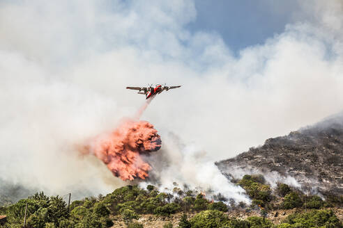 Löschflugzeug wirft eine Ladung Flammschutzmittel auf einen Waldbrand ab, Korsika, Frankreich - DHEF00239