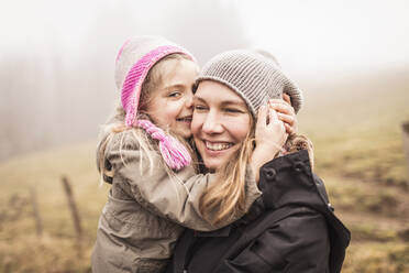Mother and daughter hugging and laughing in foggy landscape - DHEF00242