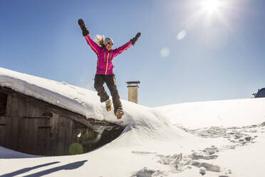 Woman jumping off the roof of a cabin into the deep snow - DHEF00257