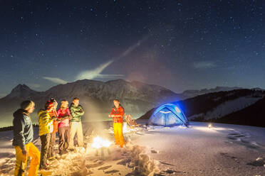 Nachtlandschaft mit glühendem Zelt im Schnee und Menschen am Feuer, Achenkirch, Österreich - DHEF00260