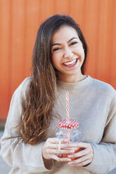 Cheerful young woman with long brown holding drink - JMPF00325