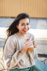 Cheerful young woman with long brown holding drink - JMPF00328