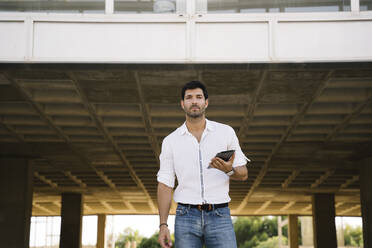 Selbstbewusster Geschäftsmann mit digitalem Tablet beim Spaziergang in der Stadt - MPPF01022