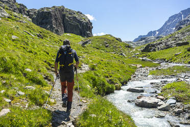 Mann beim Wandern am Bach auf einem Berg in den westlichen Rätischen Alpen, Sondrio, Italien - MCVF00566