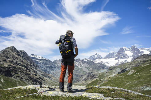 Mann bewundert die Aussicht, während er auf einem Berggipfel in den westlichen Rätischen Alpen steht, Sondrio, Italien - MCVF00568