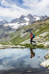 Man walking by lake with reflection at Western Rhaetian Alps Sondrio, Italy - MCVF00571