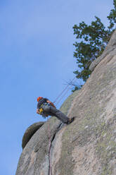 Von unten Mann klettert mit Kletterausrüstung auf einen Felsen in der Natur - ADSF10721