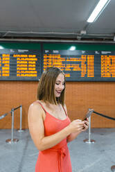 Junge Frau schreibt Textnachrichten auf ihrem Smartphone, während sie am Bahnhof steht - JMPF00331