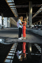 Couple standing face to face by reflection on puddle in city - JMPF00343