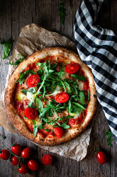 From above delicious pizza with tomato and salad placed with checkered towel on wooden background - ADSF10783