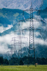 Industrielandschaft mit Stromleitungen in nebligen steinigen Bergen unter weißen Wolken in Blau in Österreich - ADSF10788