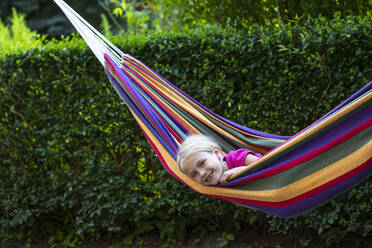 Smiling girl relaxing in colorful hammock at garden - JFEF00962