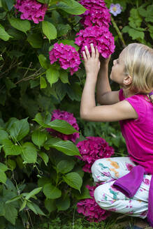 Niedliches kleines Mädchen betrachtet Blumen im Garten - JFEF00965