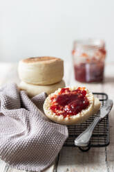 Appetizing freshly baked bun cut in half with homemade strawberry jam placed on metal grid with gray cloth and knife on kitchen table - ADSF10796