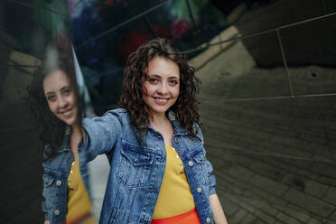 Porträt einer lächelnden jungen Frau, die vor einer Spiegelwand steht - OGF00456