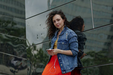 Young woman using smartphone leaning on wall - OGF00458