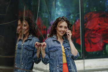 Junge Frau mit Smartphone an der Wand lehnend - OGF00461